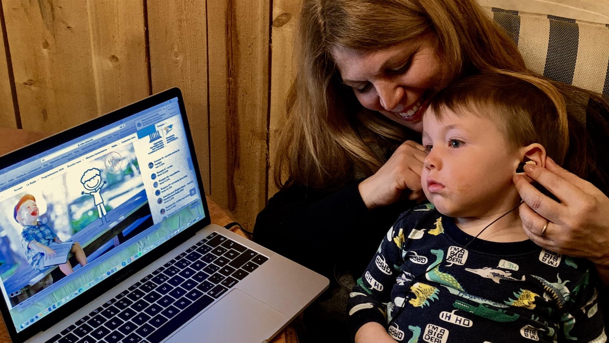 Un enfant en pyjama sur les genoux de sa mère qui écoute la radio avec des écouteurs.