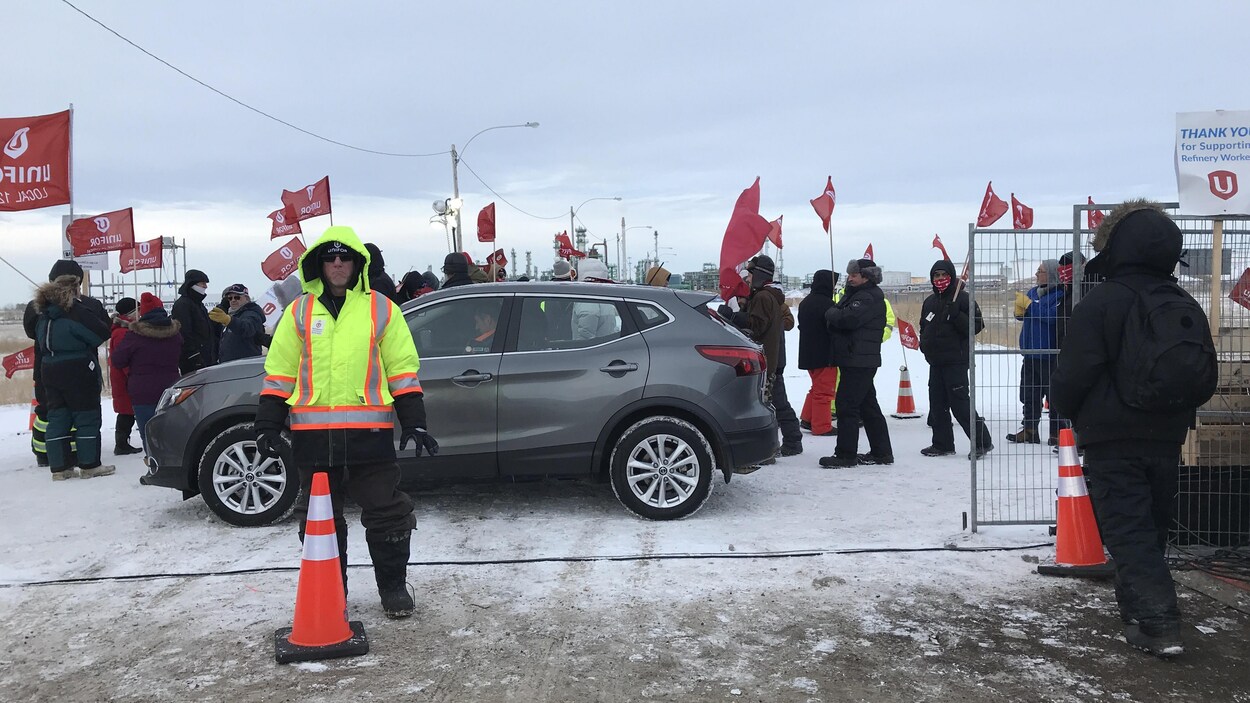 Des gens, à l'extérieur, marchent avec des drapeaux d'Unifor.
