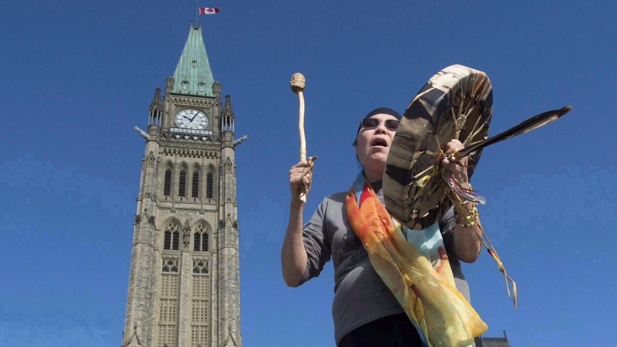 Une femme autochtone joue du tambourin devant l'édifice du Parlement à Ottawa.