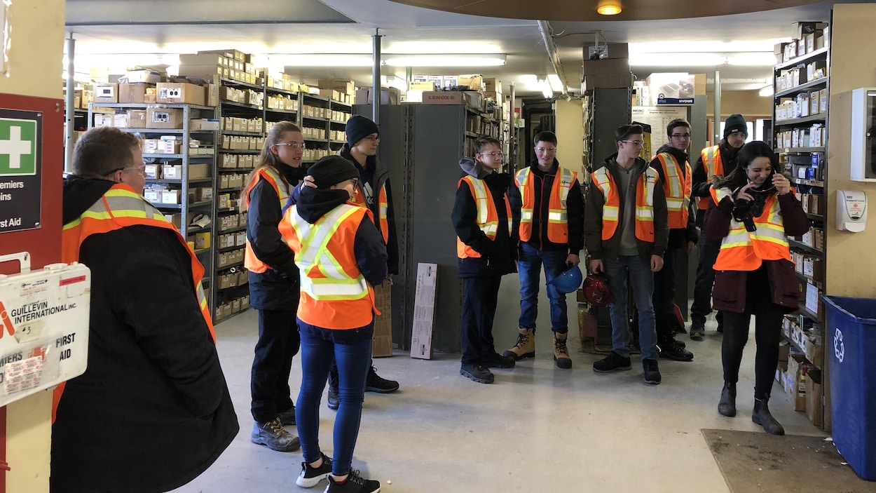 Des jeunes portant des dossards et des lunettes de sécurité visitent un entrepôt.