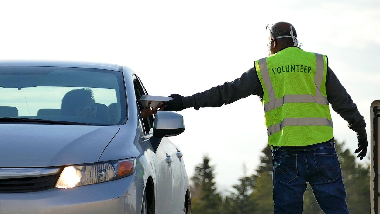 Un homme en veste qui dit « bénévole » passe un repas à un conducteur de voiture.