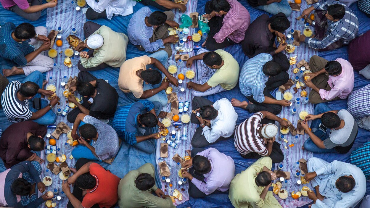 Des hommes mangent, assis sur des nappes déposées par terre, dans une mosquée lors du ramadan.