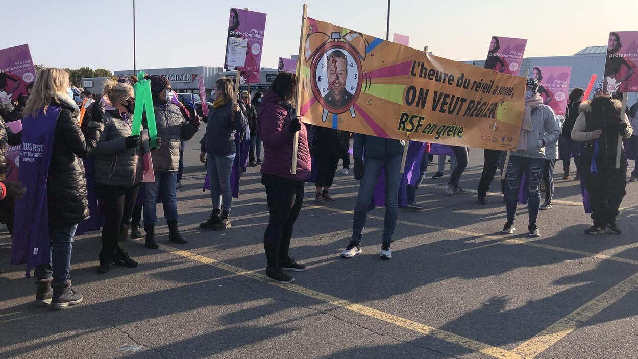 Des femmes manifestent en brandissant une banderole ornée d'une photographie du ministre québécois de la Famille, Mathieu Lacombe.