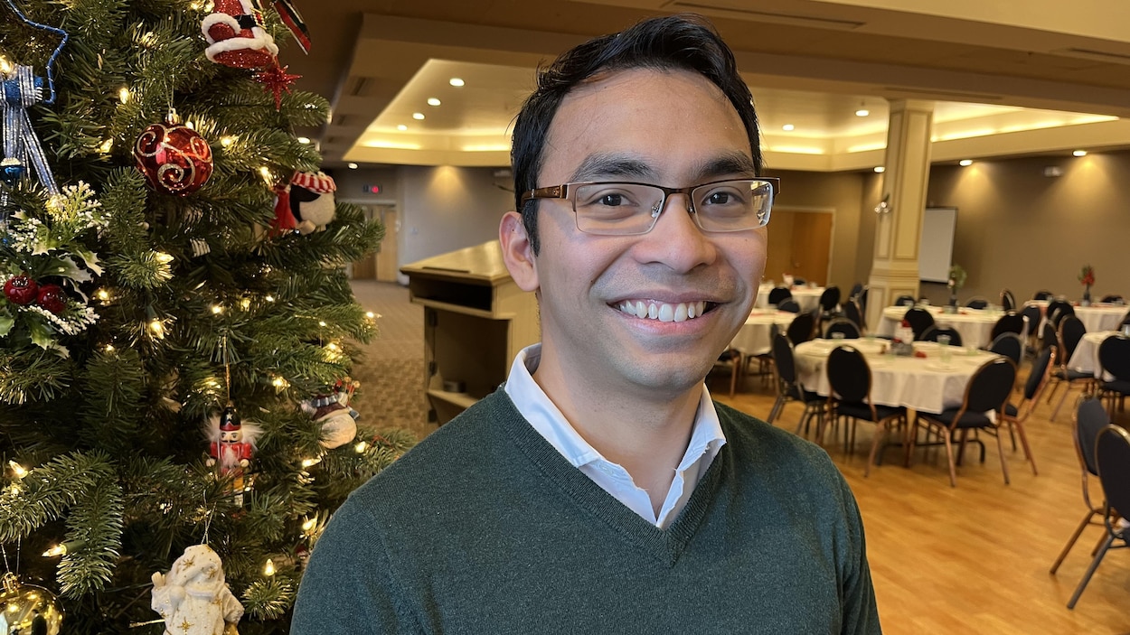 Raymart Lugue, souriant, pose pour une photo près d'un sapin de Noël décoré.