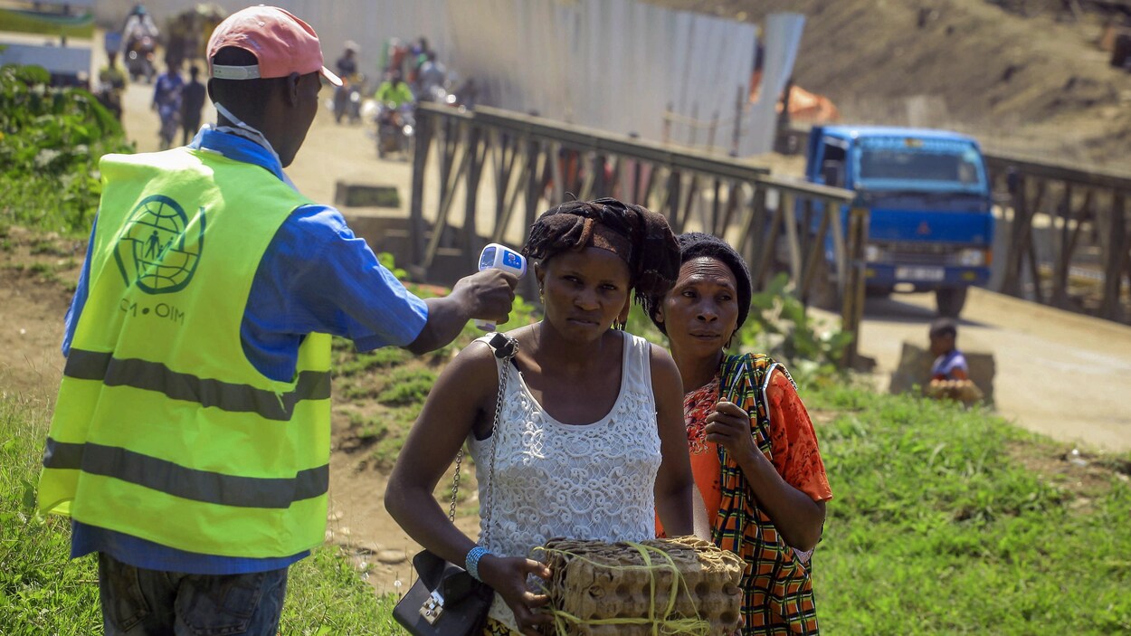 Un employé de l'OMS prend la température des personnes à la frontière entre le Congo et l'Ouganda.