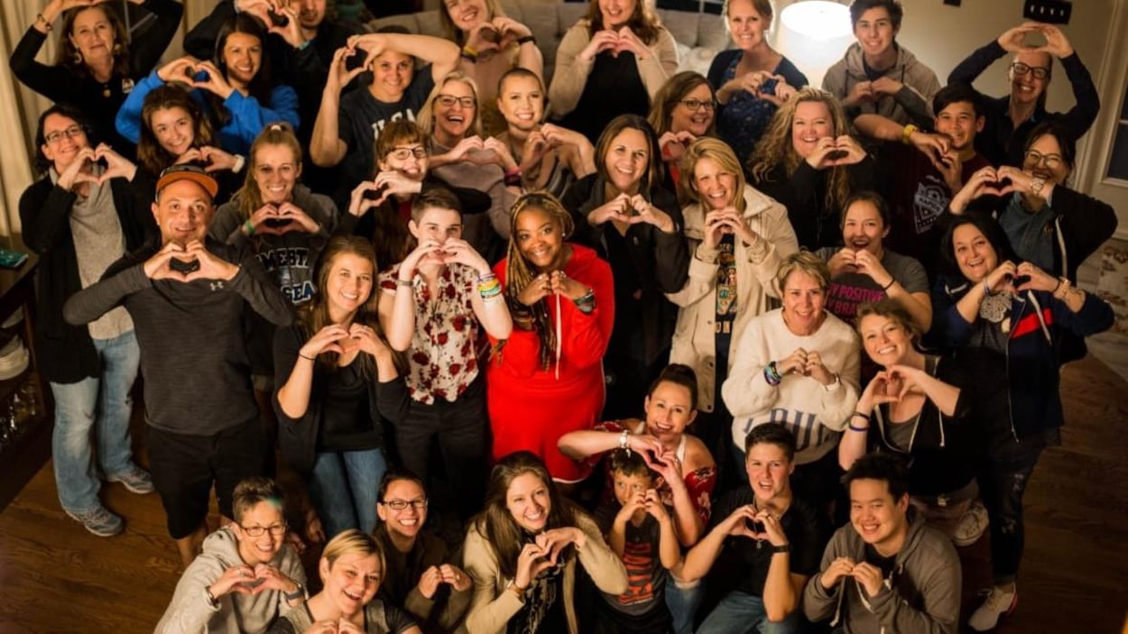 Une trentaine de personnes rassemblées mettent leurs mains en forme de coeur.