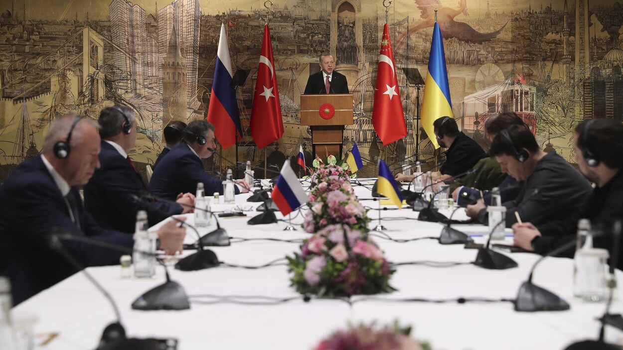 Des diplomates, assis de chaque côté de la table, écoutent le discours d'Erdogan.