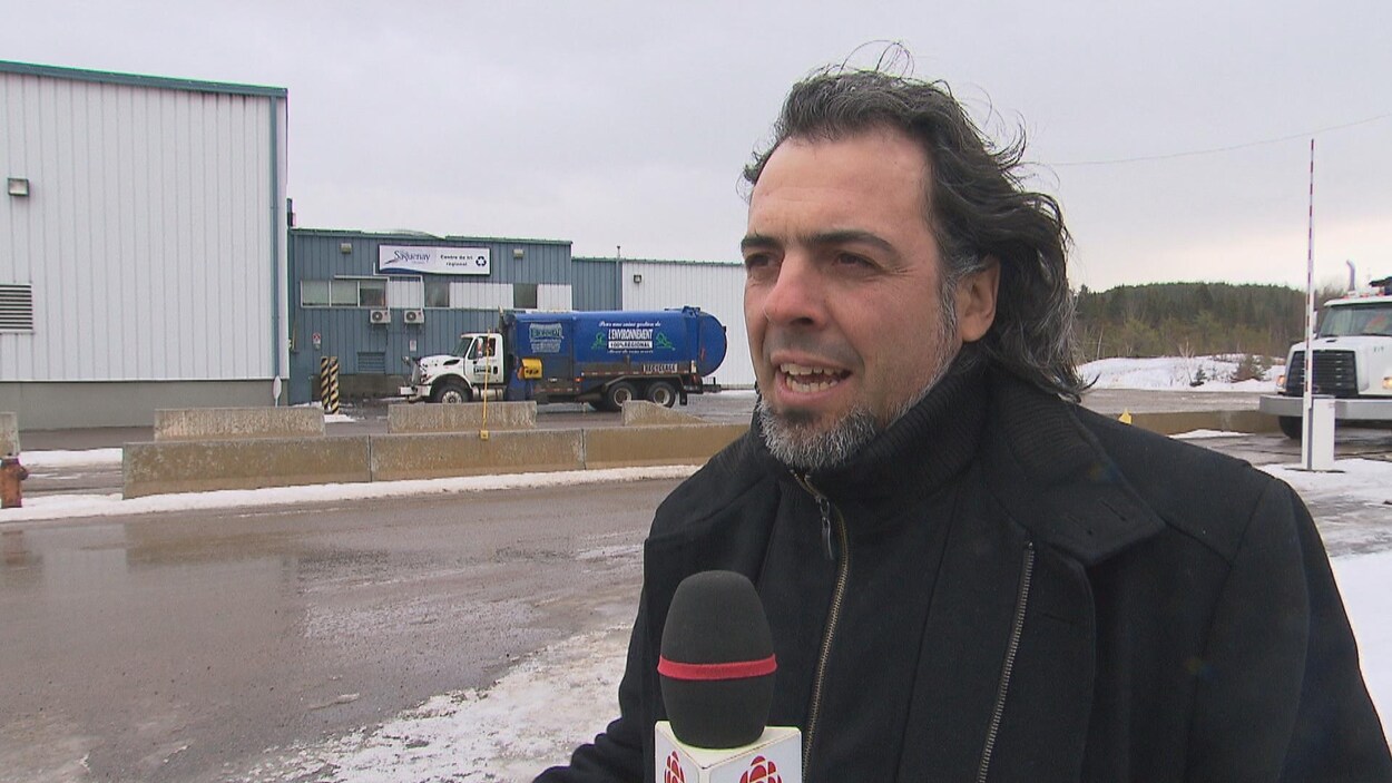 Un homme parle au micro devant un édifice et un camion de recyclage