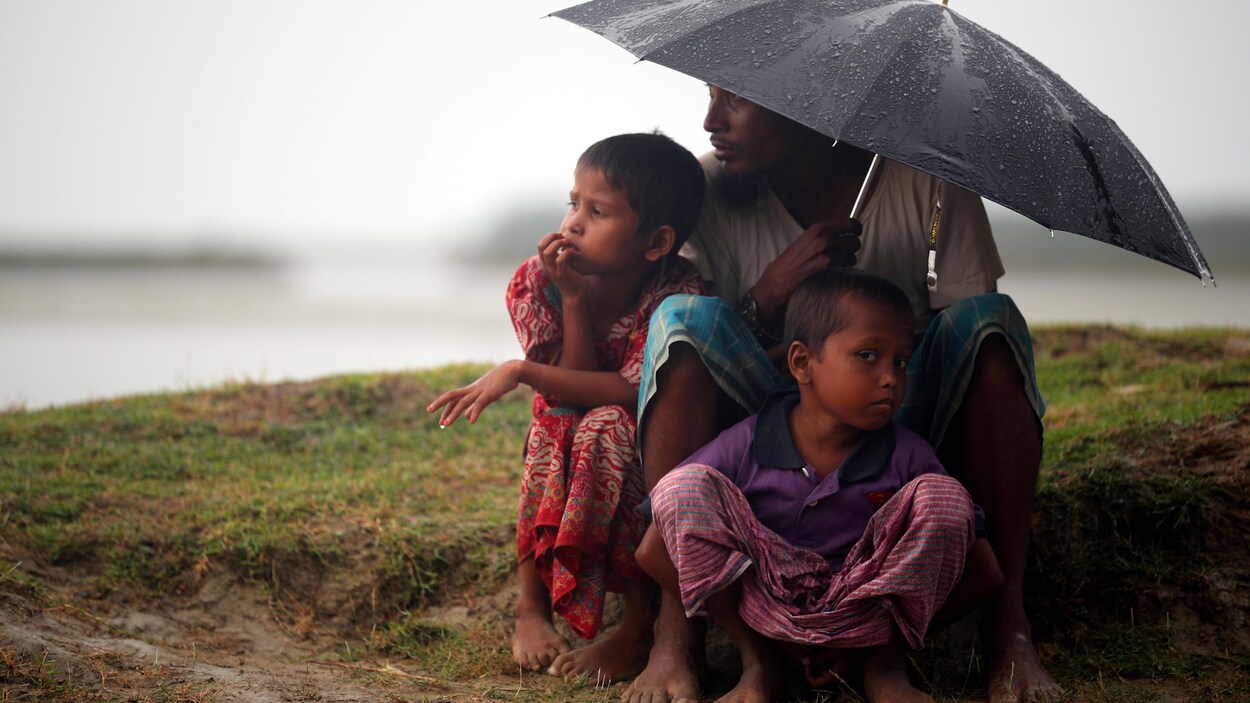 Un réfugié rohingya abrite deux enfants sous un parapluie.