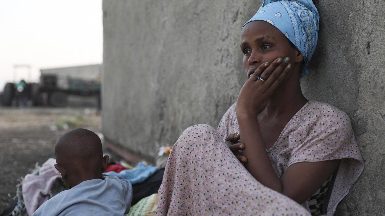 Une femme est assise par terre, adossée à un mur, près de son garçon.