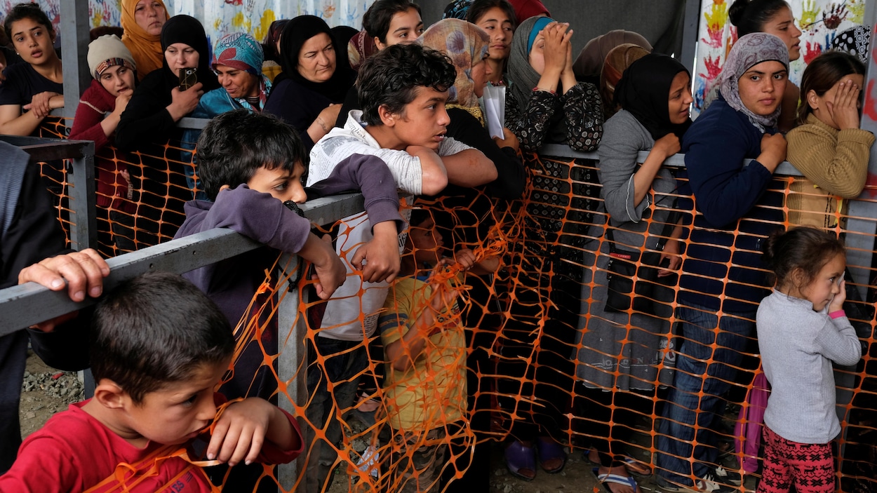 Plusieurs enfants et femmes en file derrière une barrière. Plusieurs enfants et femmes en file derrière une barrière.
