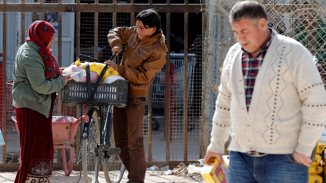 Une femme et son fils lestent de la nourriture dans un panier de bicyclette, alors qu'un homme marche devant eux avec une boîte d'aliments. Une femme et son fils lestent de la nourriture dans un panier de bicyclette, alors qu'un homme marche devant eux avec une boîte d'aliments.