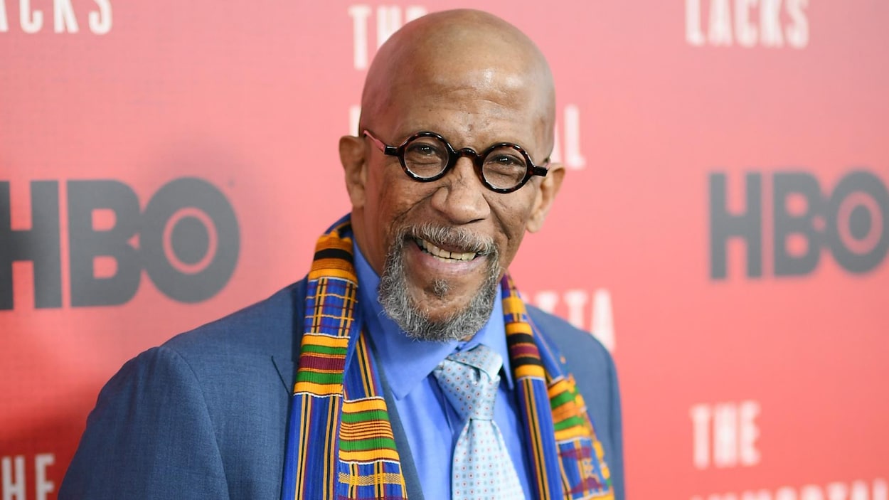 Reg E. Cathey pose lors d'un tapis rouge, en costume bleu, un foulard coloré autour du cou. Reg E. Cathey pose lors d'un tapis rouge, en costume bleu, un foulard coloré autour du cou.