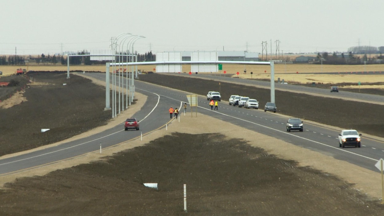 Une nouvelle intersection d’autoroute, parcourue par quelques voitures ainsi que quelques piétons portant des vestes de sécurité à haute visibilité.