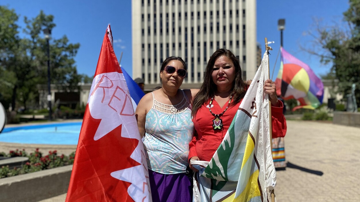 Kerry Bellegarde Opoonechaw et Star Andreas posent devant l'hôtel de ville de Regina en tenant des drapeaux du Canada et du traité numéro 4.