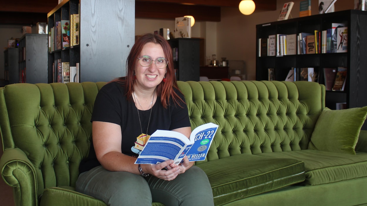 Annabel Townsend, assise sur un canapé vert dans sa librairie, lit un livre.