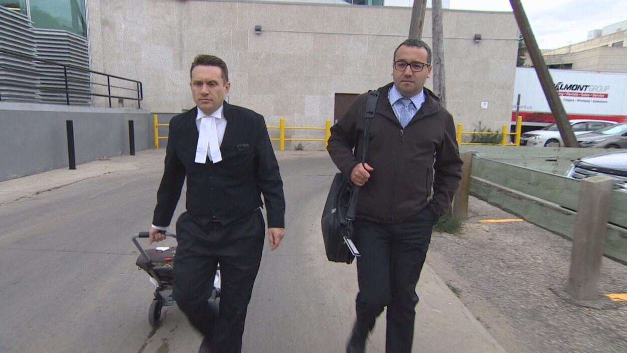Deux hommes vêtus de noir marchent à l'extérieur.