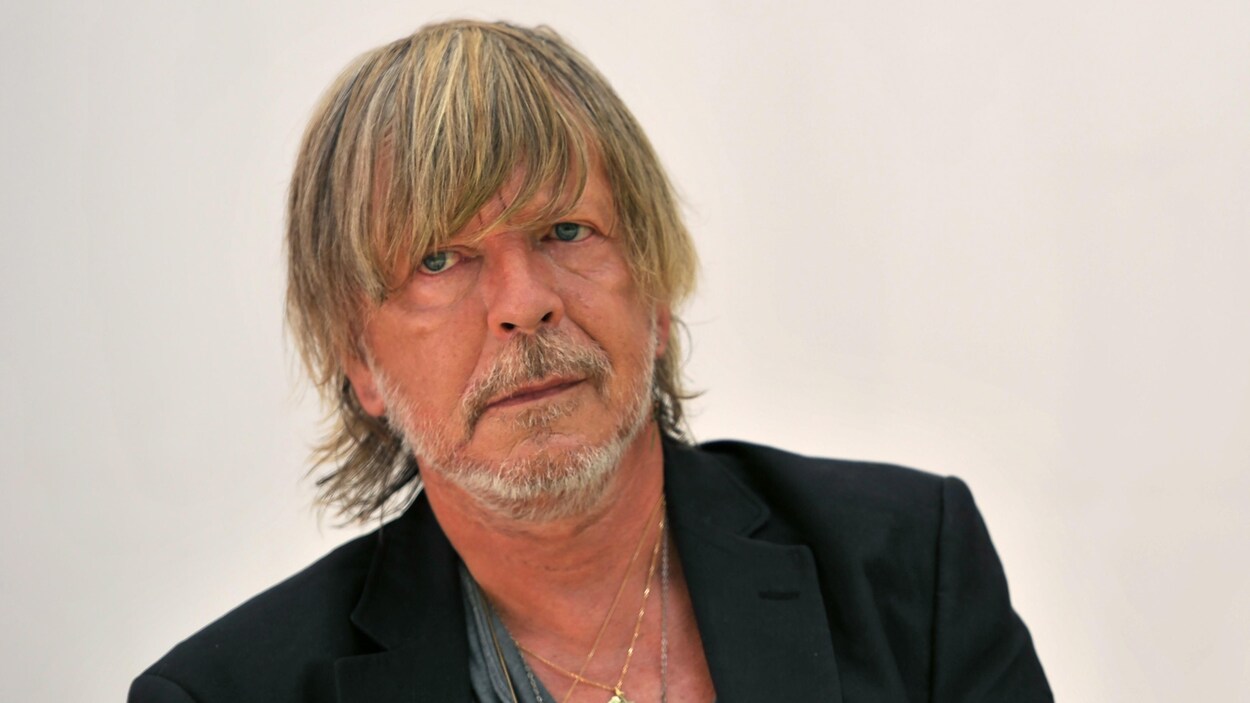 Le chanteur français Renaud porte un veston noir et plusieurs chaînes en or au cou.