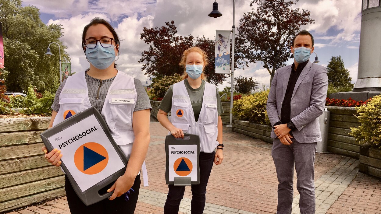 Trois intervenants posent pour la caméra. Ils tiennent un livret dans leur main indiquant psychosocial.