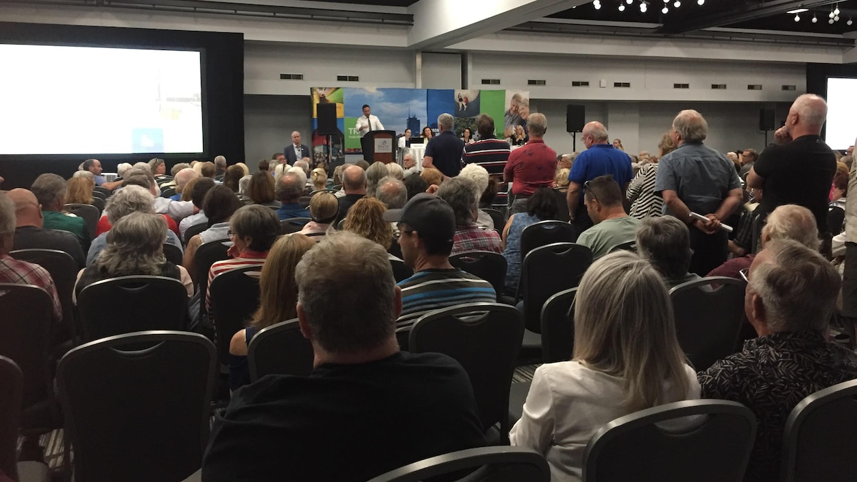 Des gens debout au micro et d'autres assis sur des chaises dans une salle du centre des congrès.