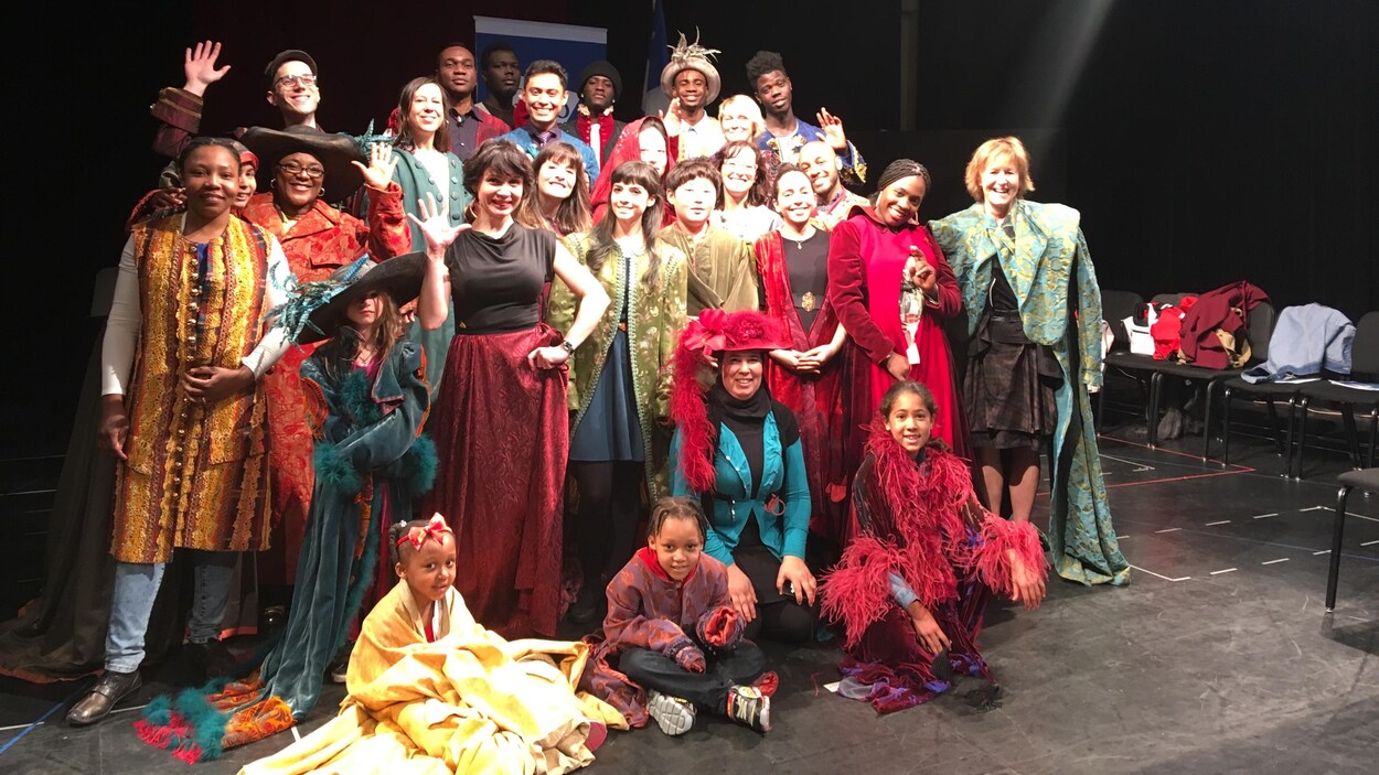 Plusieurs personnes dont des immigrants montréalais sourient lors d'une photo de groupe sur la scène d'un théâtre.