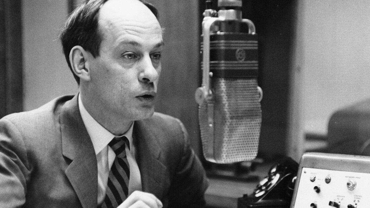 Dans un studio de radio, assis à une table et devant un micro suspendu, l'animateur René Lévesque. Dans un studio de radio, assis à une table et devant un micro suspendu, l'animateur René Lévesque.
