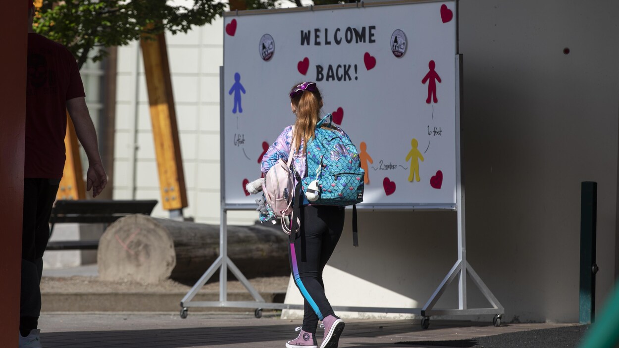 Jeune fille avec un sac sur le dos devant une affiche souhaitant un bon retour à l'école.