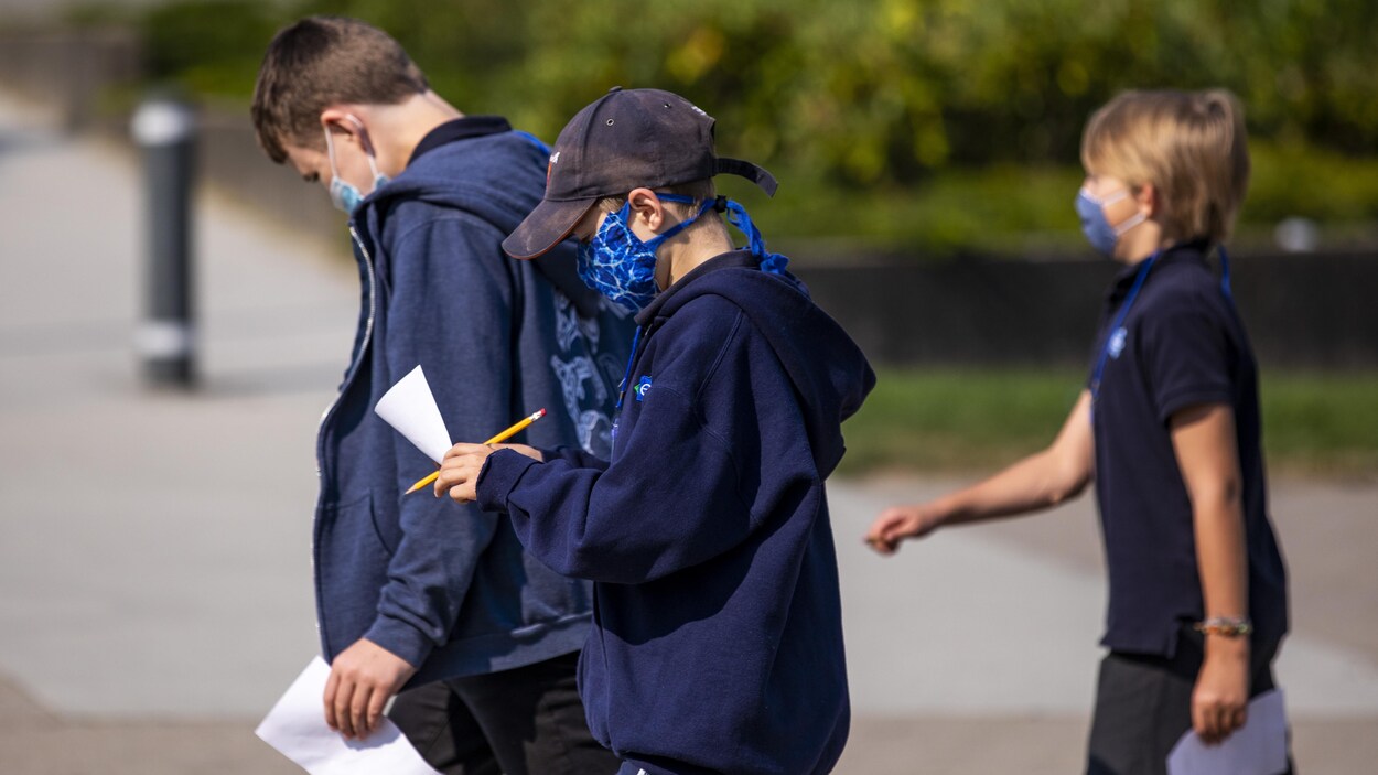 Trois garçons qui portent des masques arrivent à l'école.