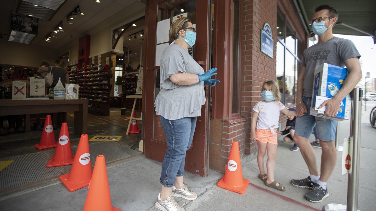 Un homme et sa fille portant un masque attendent pour entrer dans un magasin.
