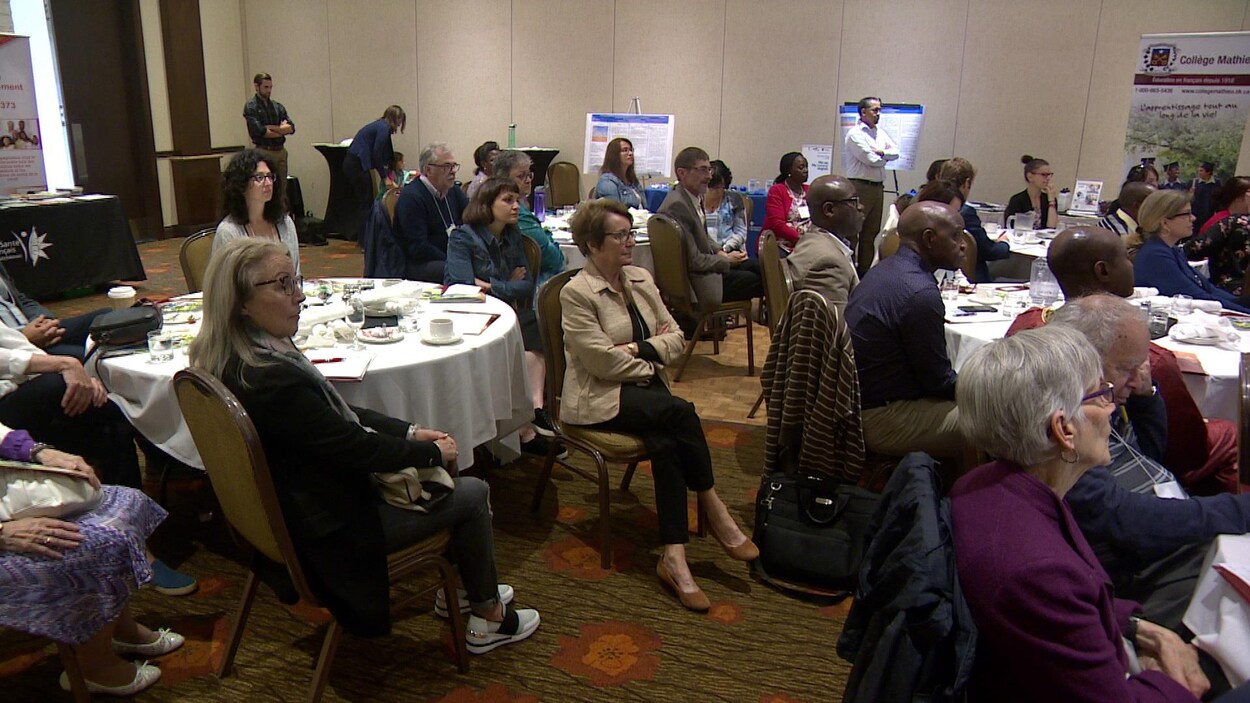 Une vingtaine de personnes sont assises autour de plusieurs tables en train d'écouter un discours lors de la réunion du Réseau santé en français de la Saskatchewan.