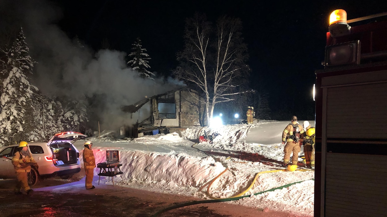 Des pompiers s'affairent autour de la maison incendiée.