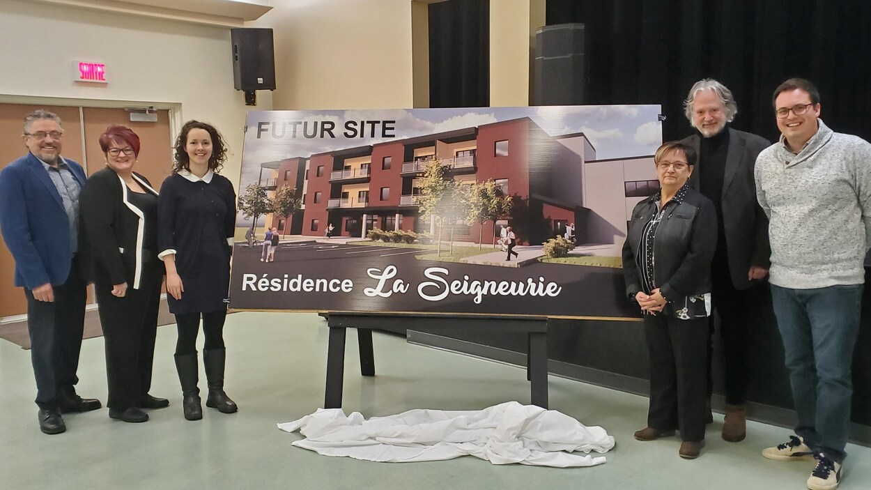 Trois hommes et trois femmes posent devant l'image d'un immeuble à logement moderne.
