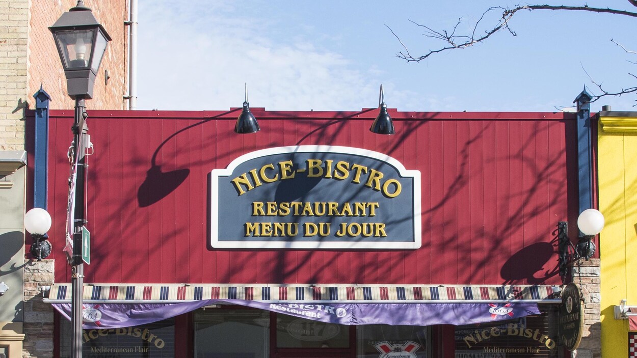 Vue de la façade principale du restaurant Nice Bistro avec l'enseigne et les lumières extérieurs, en plein jour.