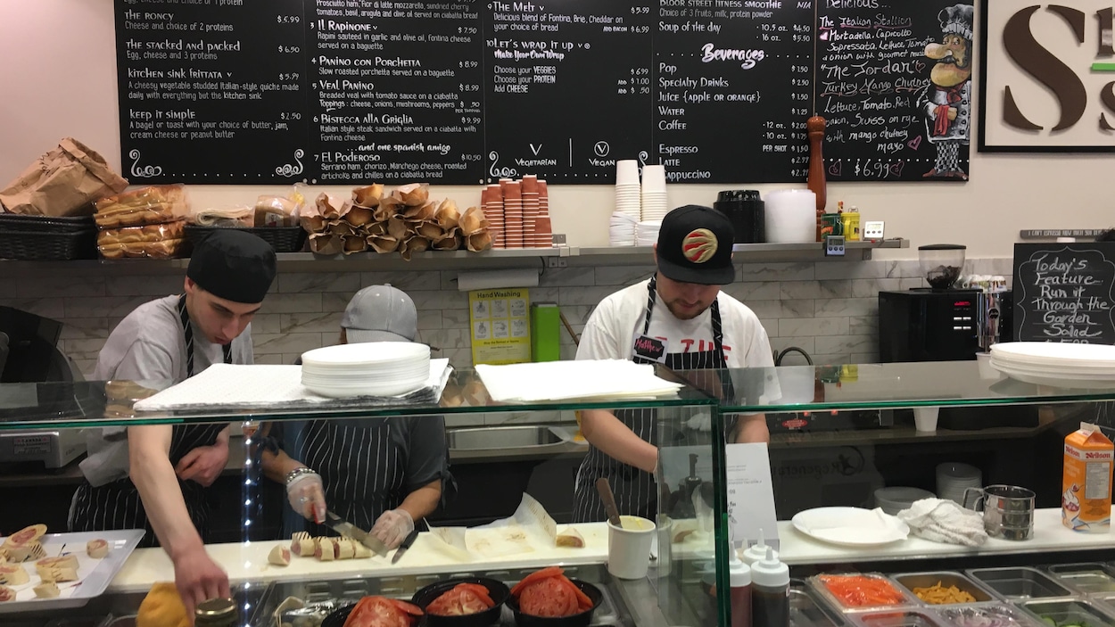 Des personnes coupent des aliments derrière le comptoir d'une sandwicherie.