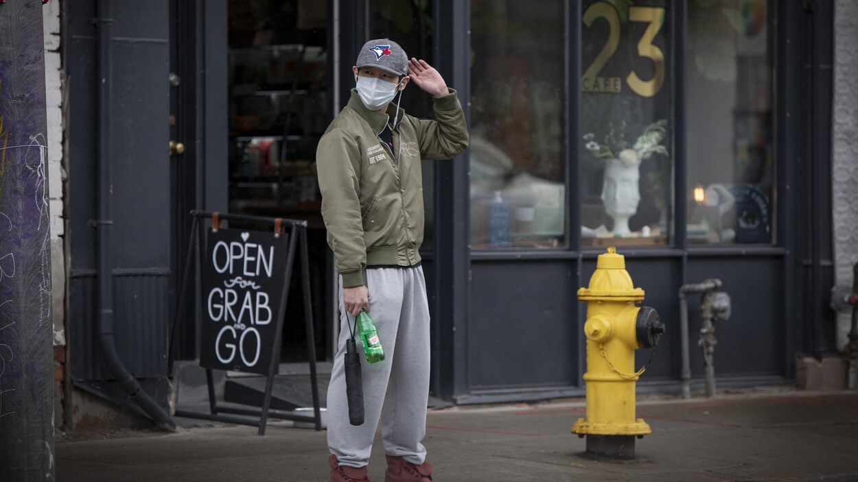 Un homme qui porte un masque se tient devant une enseigne qui précise que le restaurant derrière lui n'offre que des plats à emporter.