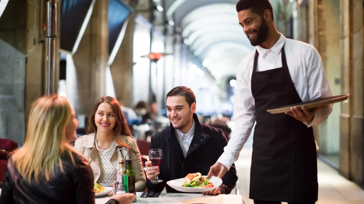 Un serveur dépose une assiette sur la table de trois clients. 