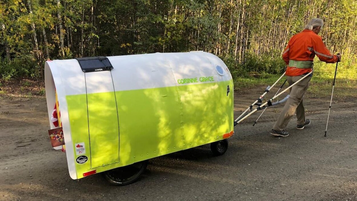 Un homme traîne une petite roulotte attachée à lui à l'aide d'un harnais.