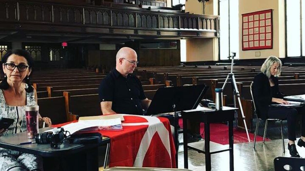 On voit trois personnes, Suzanne Steele, Neil Weisensel et Estelle Shook, assis à des tables de travail dans une église qui leur sert de lieu de travail.
