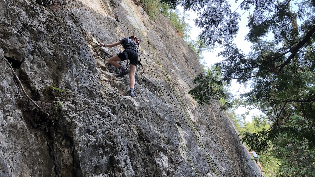 Une jeune fille escalade une parois rocheuse, près des chutes Neigette.