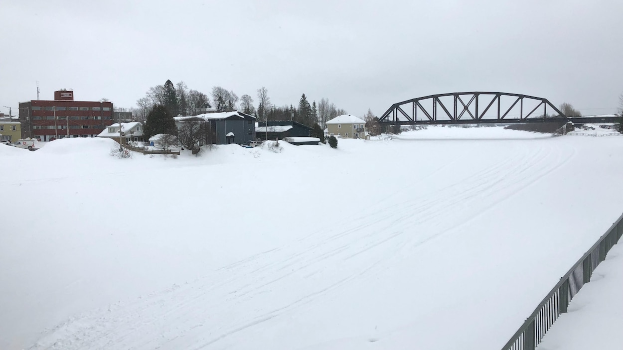 Une rivière couverte de neige, un pont de chemin de fer au loin.
