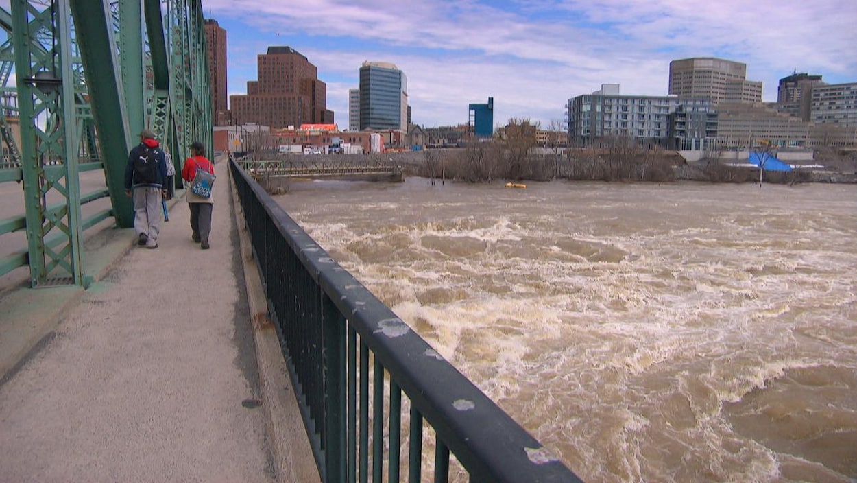 Deux piétons traversent le pont des Chaudières vers Gatineau, alors que la rivière des Outaouais gronde.