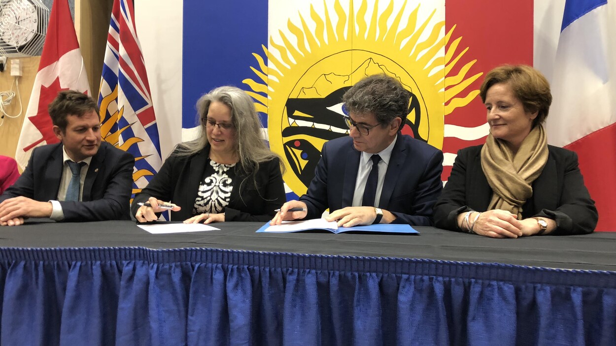 Quatre personnes assises à une table pour signer un document.
