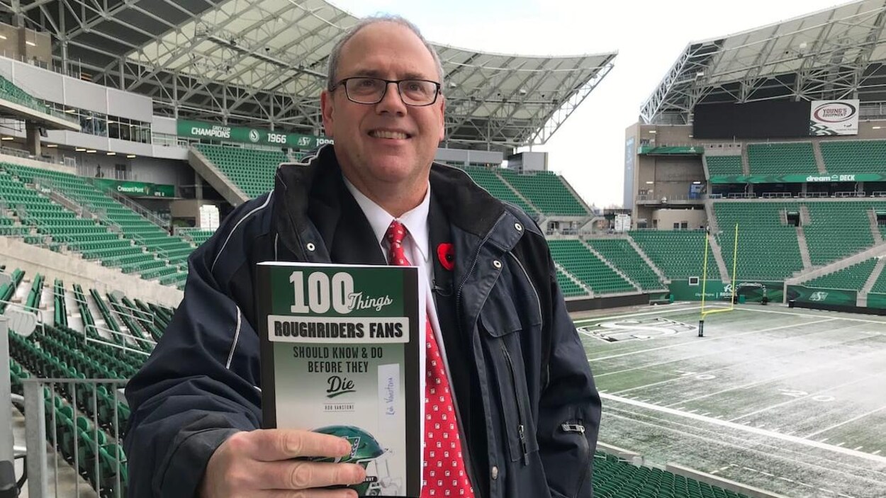 Un homme tient un livre dans un stade de football.