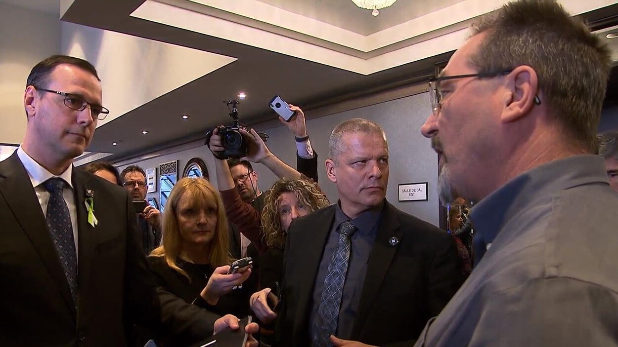Un homme se fait interpeller par un autre au milieu d'une mêlée de presse.