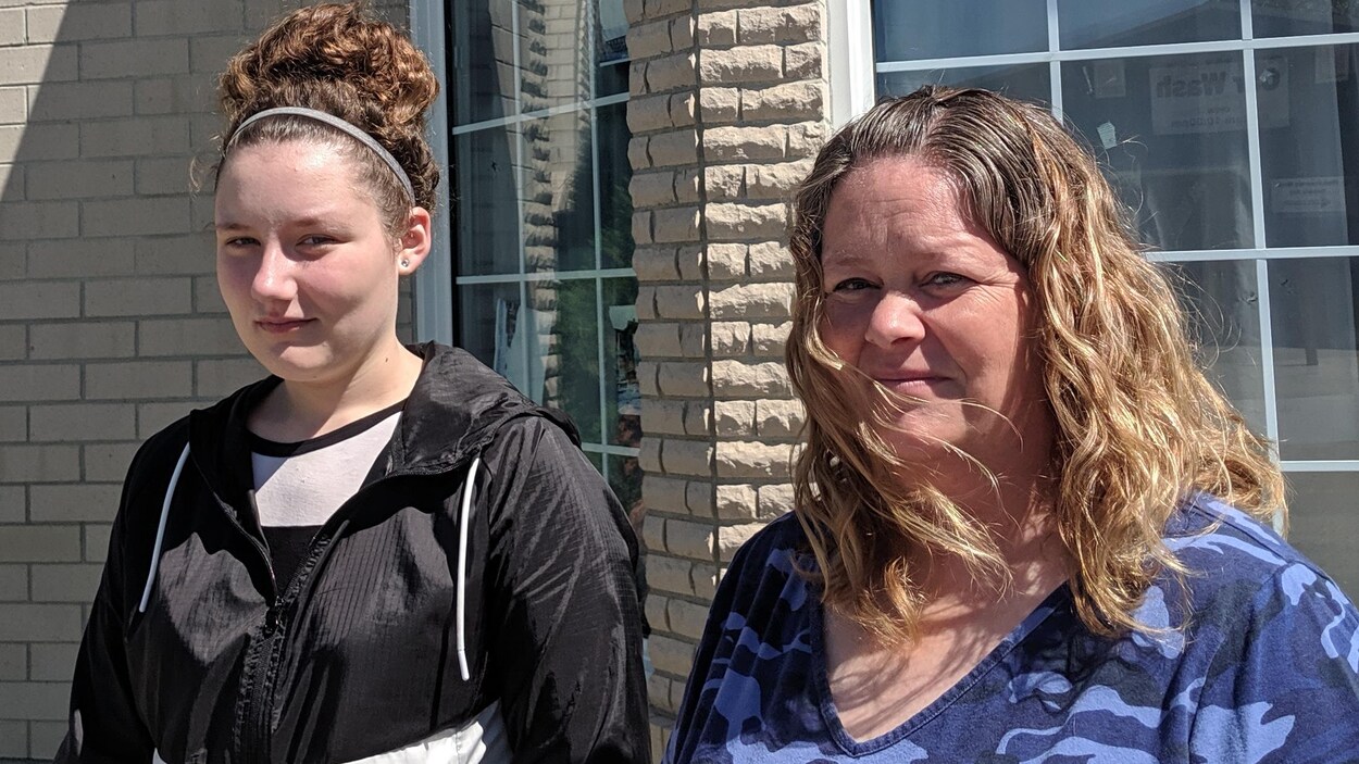 Le visage grave et l'air soucieux, Amber Thibault et sa mère, Anna Theise, posent à l'extérieur, par une belle journée ensoleillée.