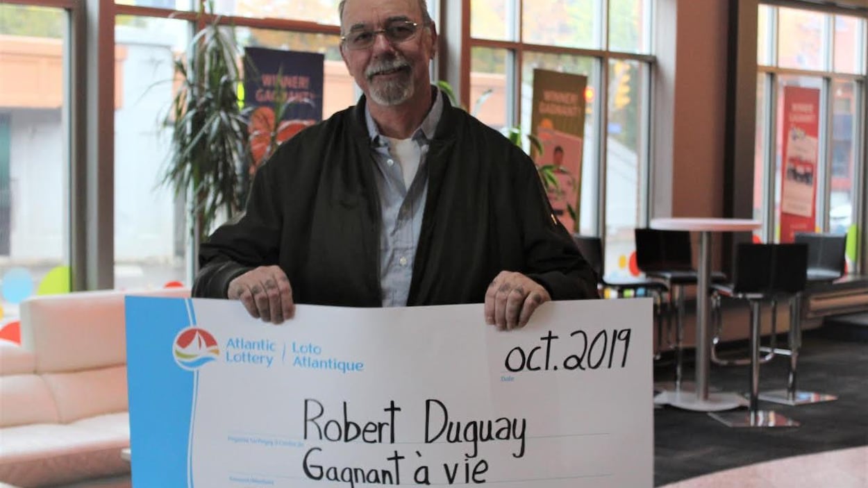 Robert Duguay, souriant, tient un chèque grand format qui l'identifie comme « Gagnant à vie ».