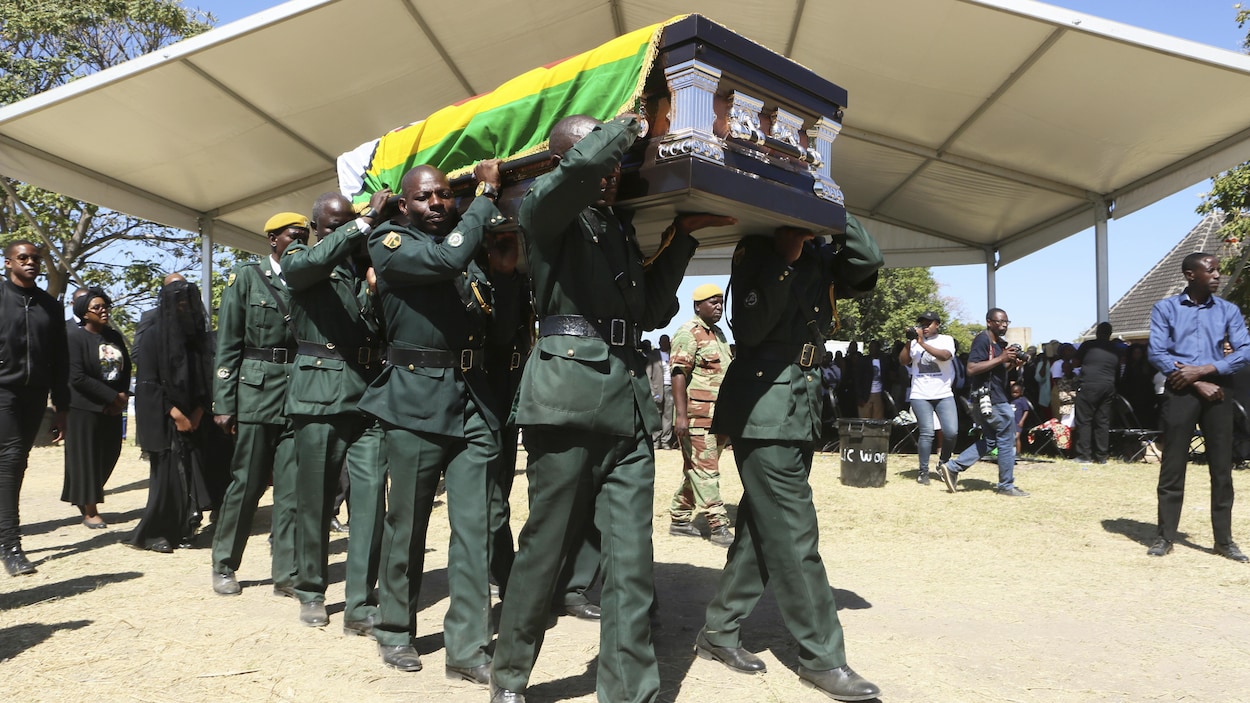 Des hommes en uniforme portent à bout de bras le cercueil de Robert Mugabe recouvert du drapeau national.