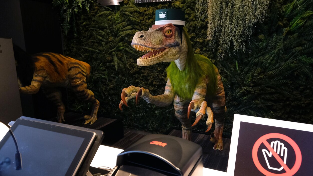 Un robot à l'apparence de vélociraptor se tient derrière un comptoir de réception à l'hôtel Henn-na.