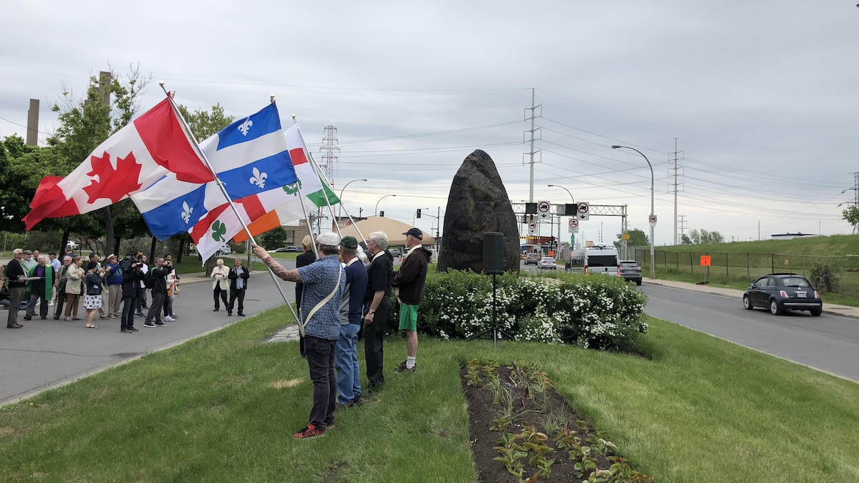Des hommes brandissent, près de la Roche noire, des drapeaux canadien, québécois, montréalais et irlandais.