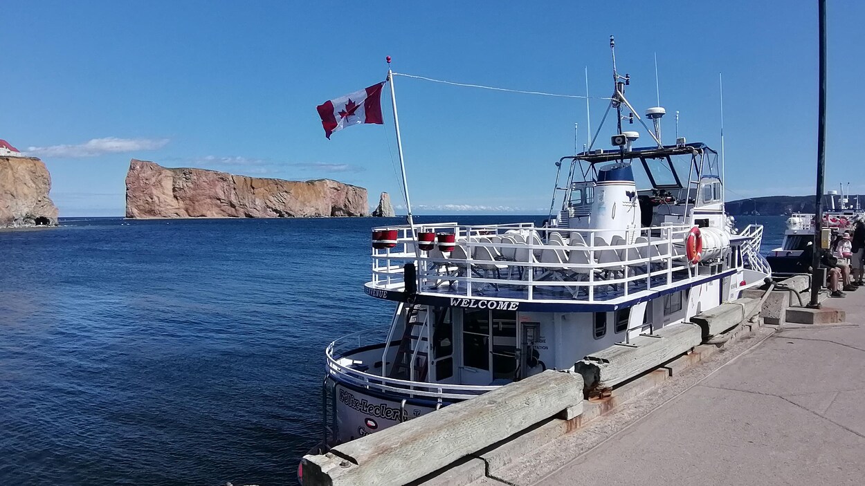 Un bateau de croisière est amarré à un quai. À l'arrière-plan, pas très loin du quai, se trouve le Rocher Percé.